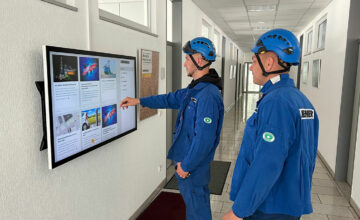 Mitarbeitende aus der Produktion holen sich die Informationen aus der LOLYO Mitarbeiter-App über den Info-Touchscreen