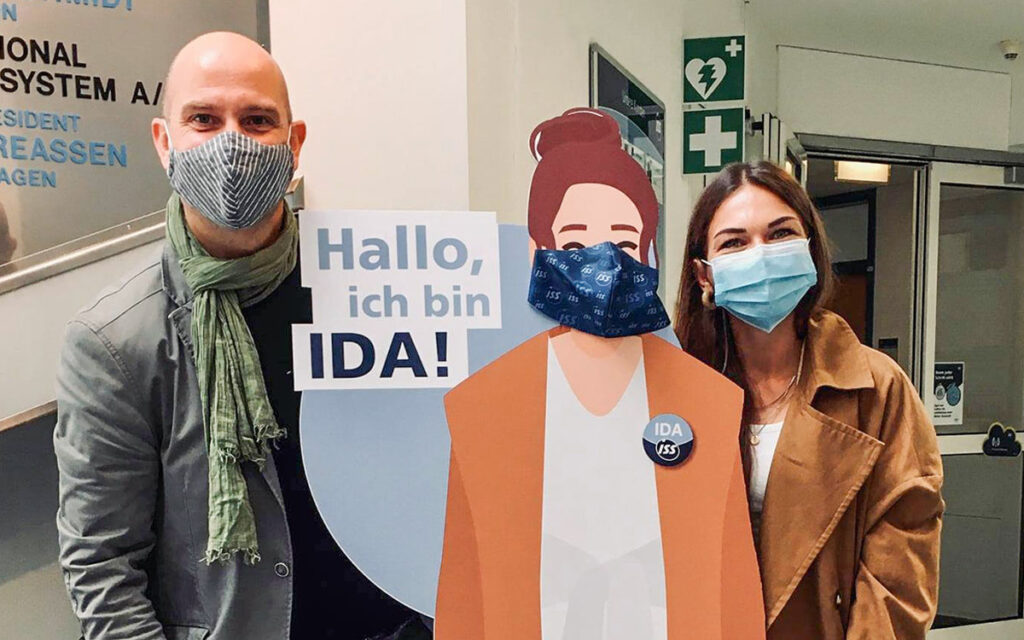 Team di lolyo con mascherine protettive insieme alla figura di cartone che rappresenta la mascotte dell'intranet mobile chiamata IDA per ISS Austria.